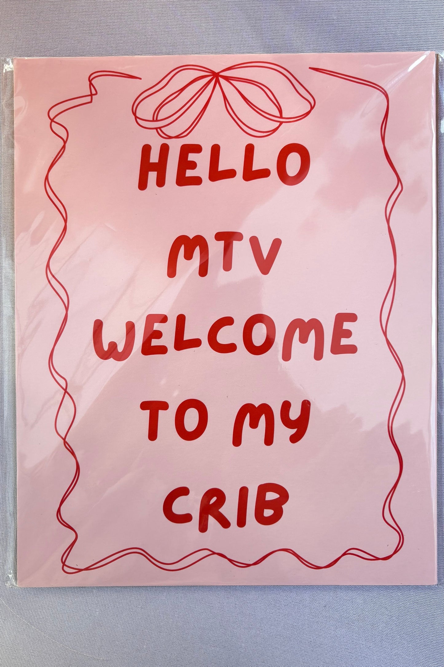 Pink sign with red text 'HELLO MTV WELCOME TO MY CRIB' on a light gray background